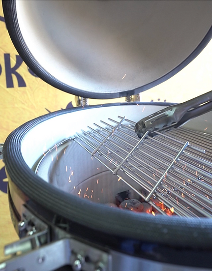 Kamado grill with open lid showing glowing coals and a metal grate.
