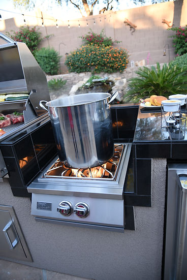 Outdoor kitchen with a pot on a stove, surrounded by plants and a wall.