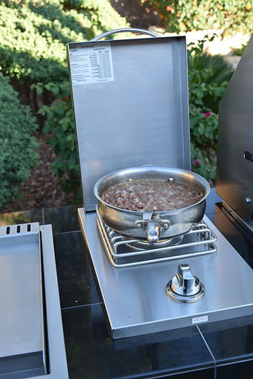 Outdoor cooking setup with a single side burner and pan on a patio