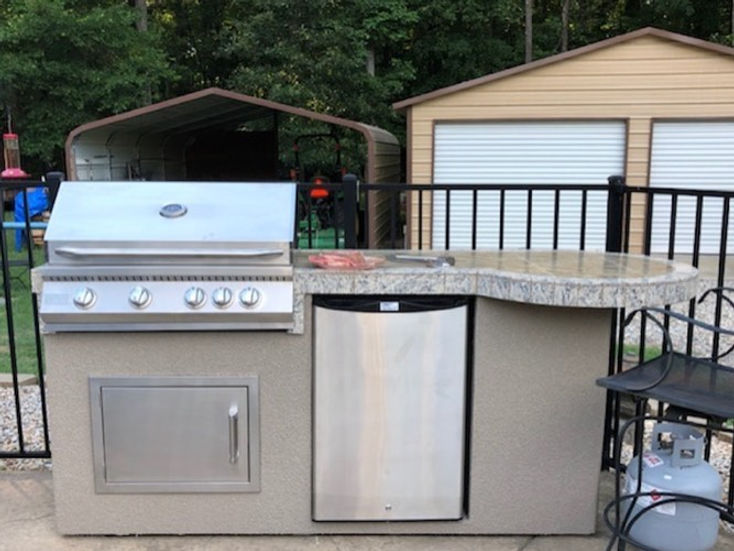 Outdoor kitchen setup with grill and refrigerator on a patio