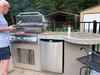 Man grilling on an outdoor kitchen with a grill and refrigerator.