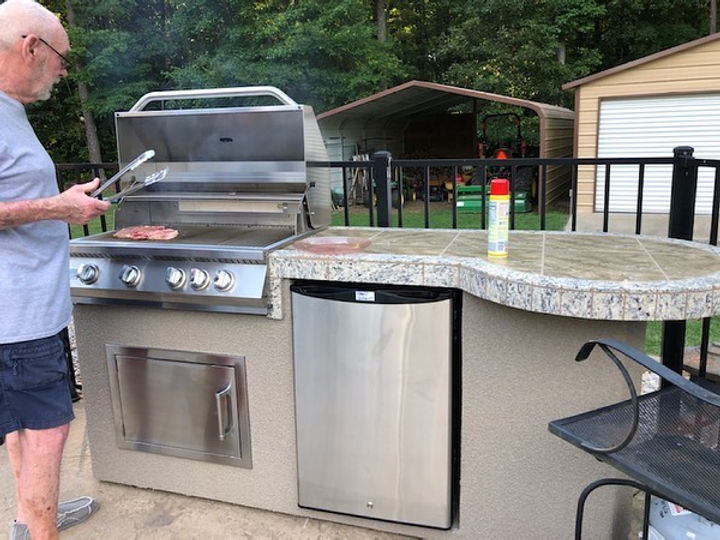 Man grilling on an outdoor kitchen with a grill and refrigerator.