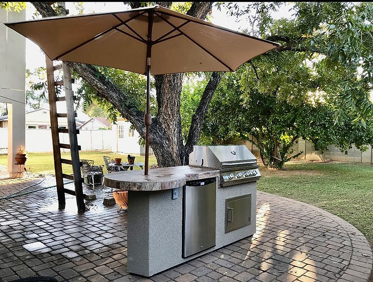 Outdoor kitchen setup with grill, table, and umbrella in a backyard setting.