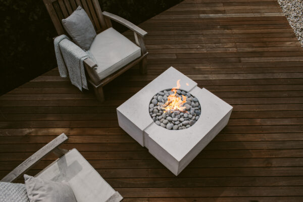 Fire pit table with flames on a wooden deck, surrounded by chairs with cushions.