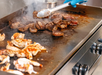 Grilling shrimp and meat on a griddle with tongs