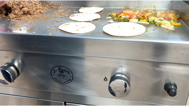 Stainless steel griddle with food items on a commercial kitchen surface