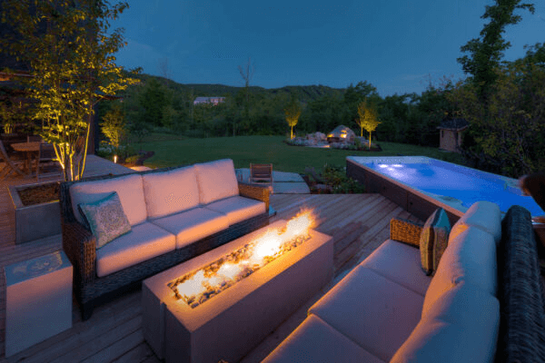 Outdoor evening setting with a fire pit, couches, and pool.