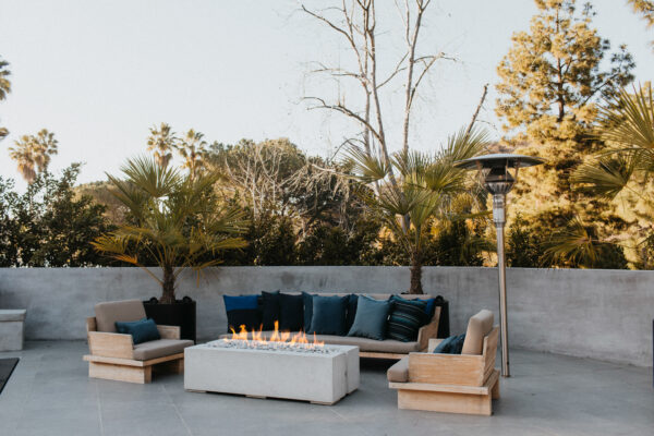 Outdoor patio with fire pit, chairs, and a heater on a clear day.