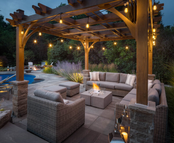 Outdoor patio with wooden pergola, seating area, and fire pit at dusk.