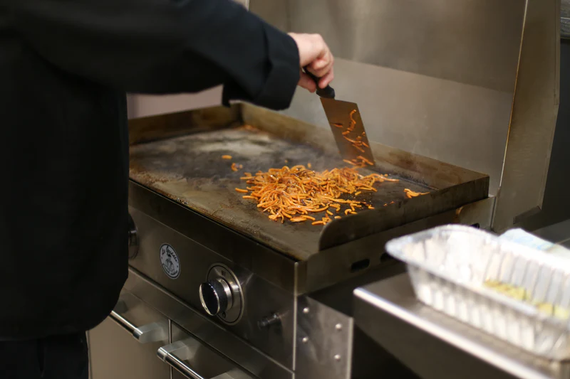 Person cooking food on a griddle with a spatula