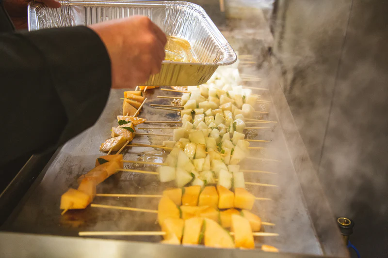 Person preparing skewered vegetables on a grill with a focus on food preparation.