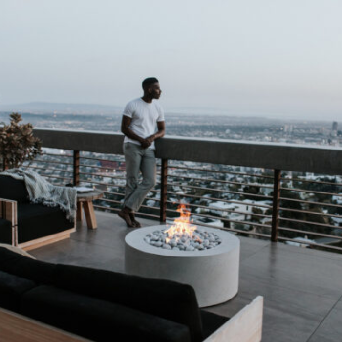 Person standing on a balcony with a fire pit and cityscape view