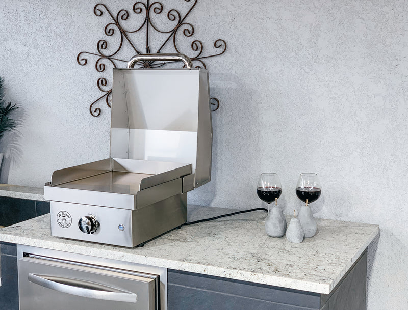 Stainless steel grill on a kitchen counter with two wine glasses and decorative elements.