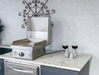 Stainless steel grill on a kitchen counter with two wine glasses and decorative elements.