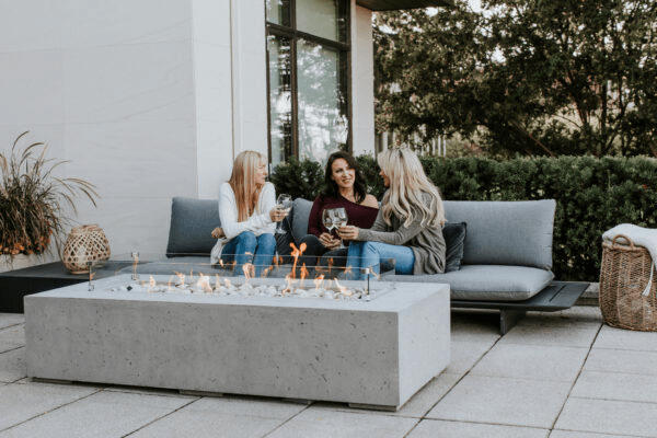 Three women sitting around a fire pit on a patio