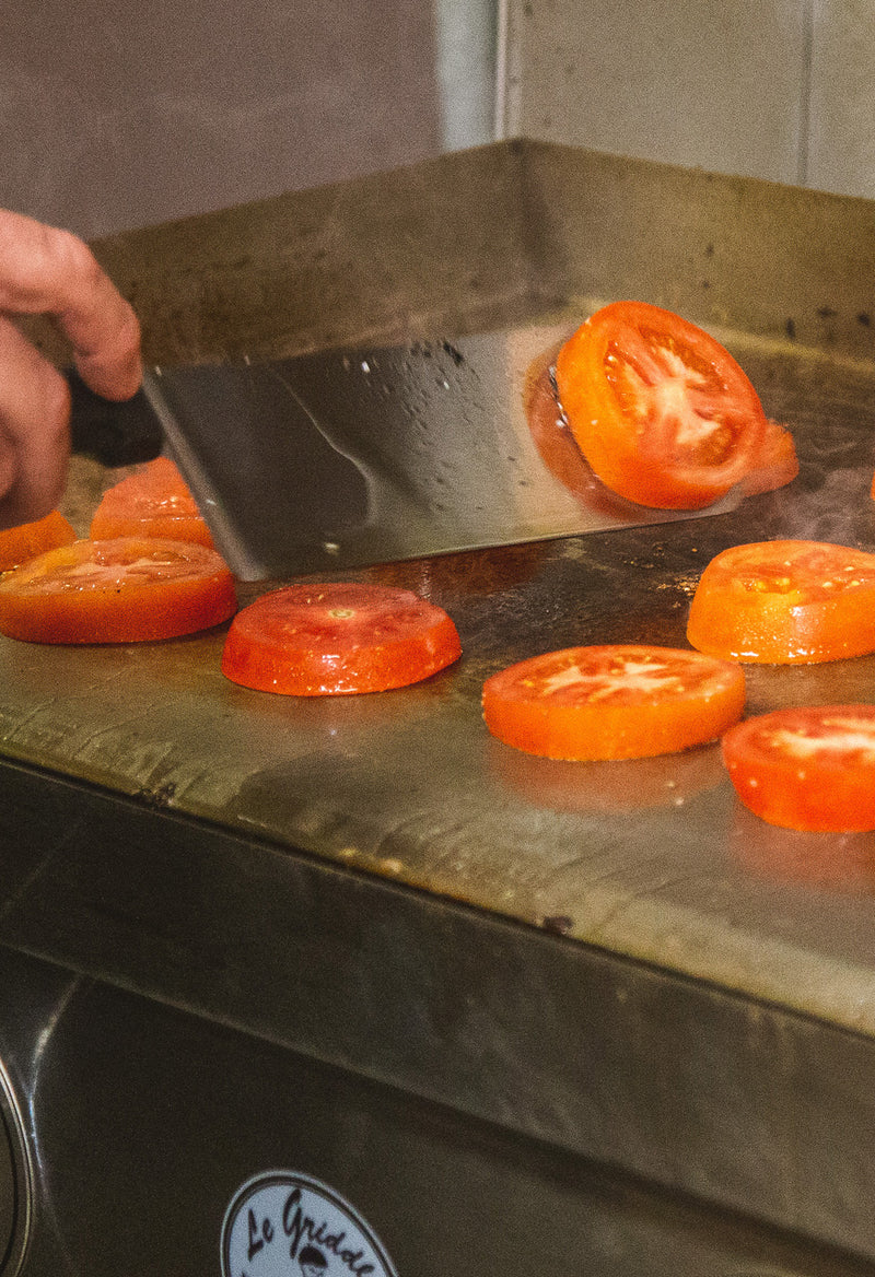 Tomatoes being flipped on a griddle