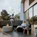 Two people on a modern rooftop patio with a fire pit and large windows.
