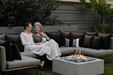 Two people sitting on a outdoor sofa with a fire pit in the foreground
