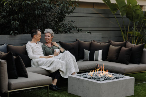 Two people sitting on a outdoor sofa with a fire pit in the foreground