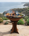 Outdoor grill with food on a patio overlooking a scenic ocean view.